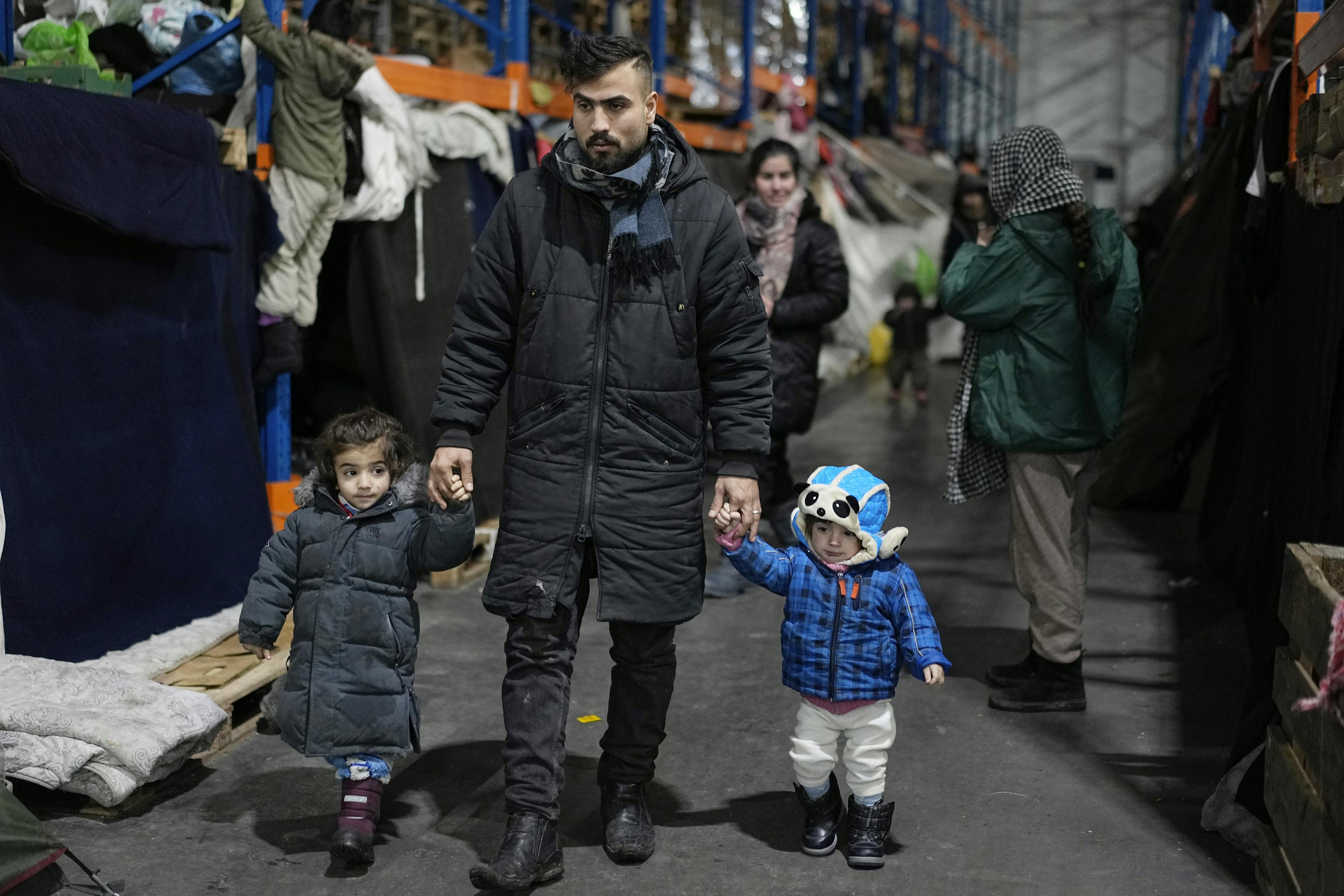 A man walks with his children as migrants settle at the checkpoint logistics center "Bruzgi" at the Belarus-Poland border near Grodno, Belarus, Thursday, Dec. 23, 2021. (AP Photo/Pavel Golovkin)